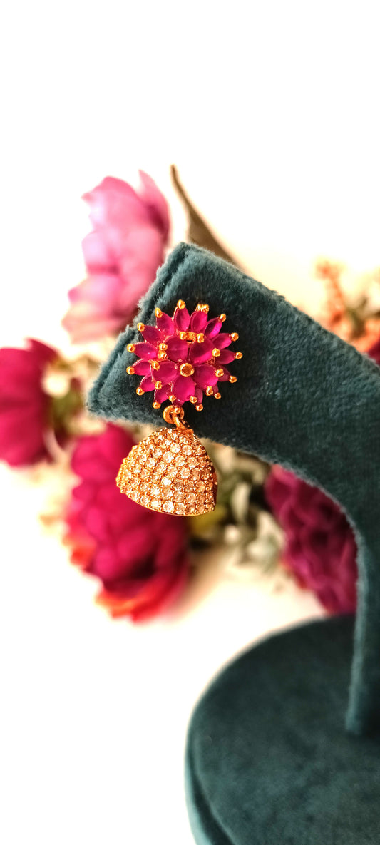 Decorative earrings on a green stand with pink flowers in the background