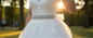 White lace wedding dress with a beaded waistband in a park setting with sunlight filtering through.