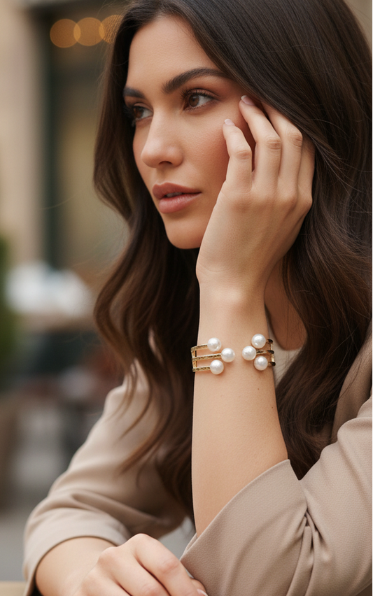 Woman sitting at an outdoor cafe table, wearing a pearl bracelet.
