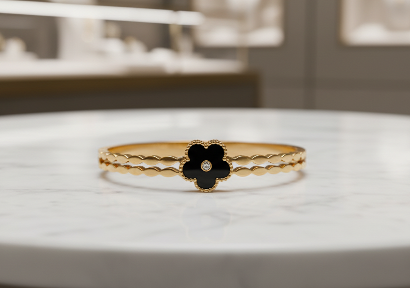 Gold bracelet with a black flower charm on a marble table in a jewelry store setting.
