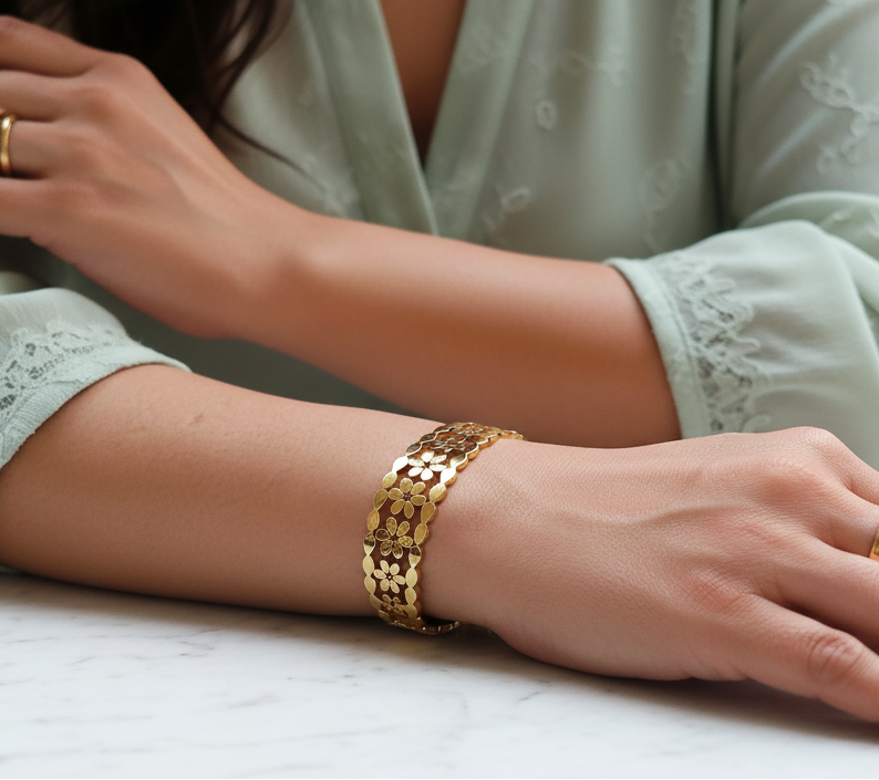 Close-up of a person's arm with a gold bracelet and rings, wearing a light green embroidered top.