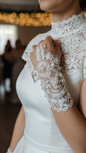 Close-up of a person wearing a white lace wedding dress with gloves.