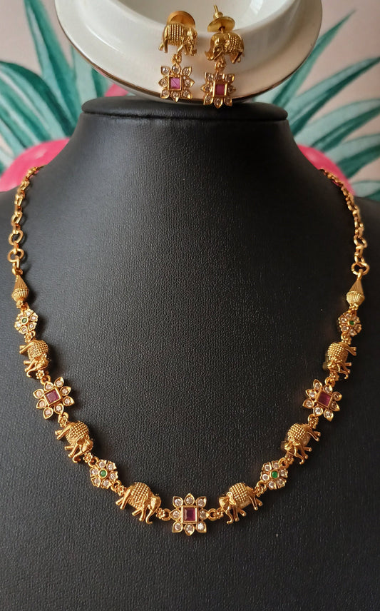Gold necklace and earrings on a black mannequin with a white bowl and green leaves in the background.