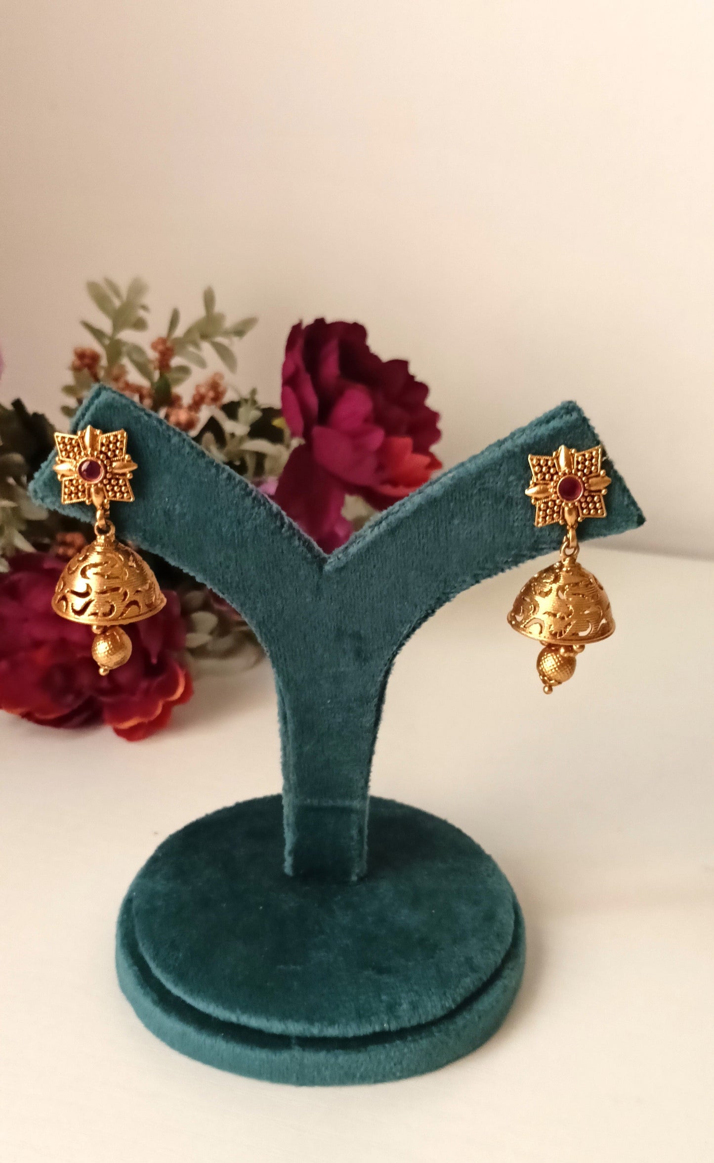 Gold earrings on a green velvet earring stand with flowers in the background