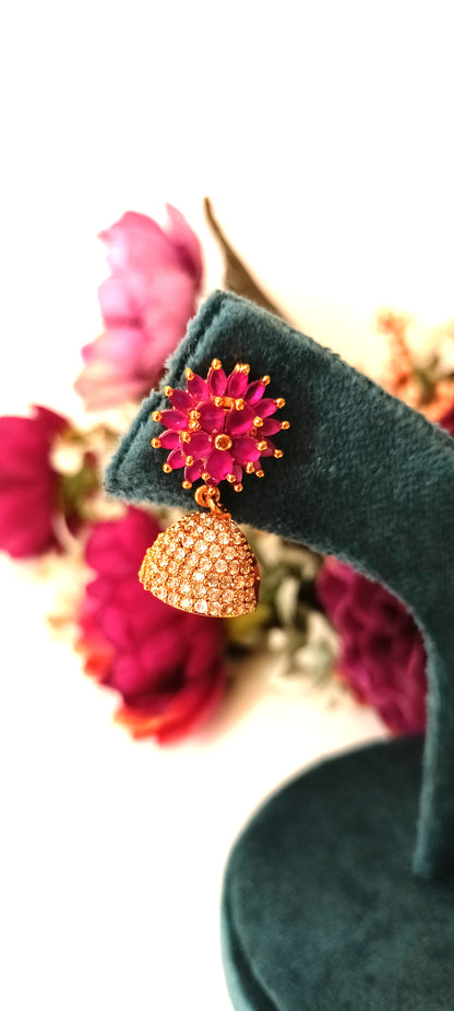 Decorative earrings on a green stand with pink flowers in the background