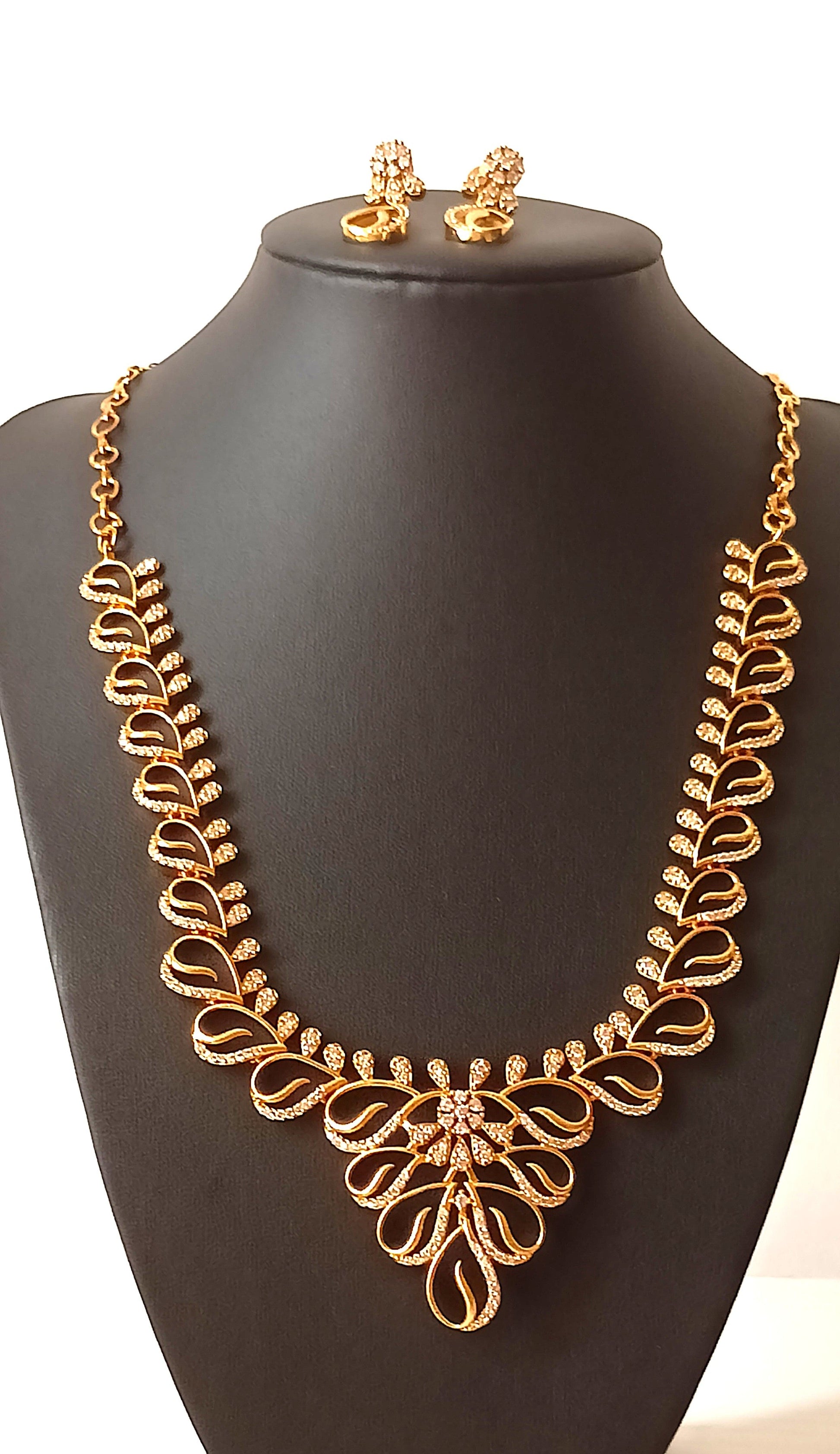 Gold necklace and earrings on a black mannequin bust with a floral background.