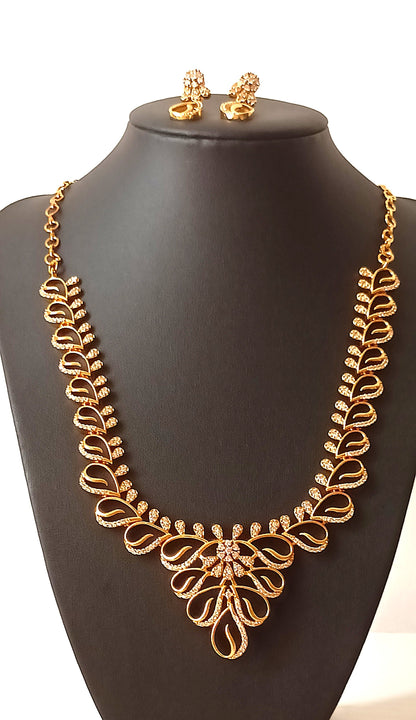 Gold necklace and earrings on a black mannequin bust with a floral background.