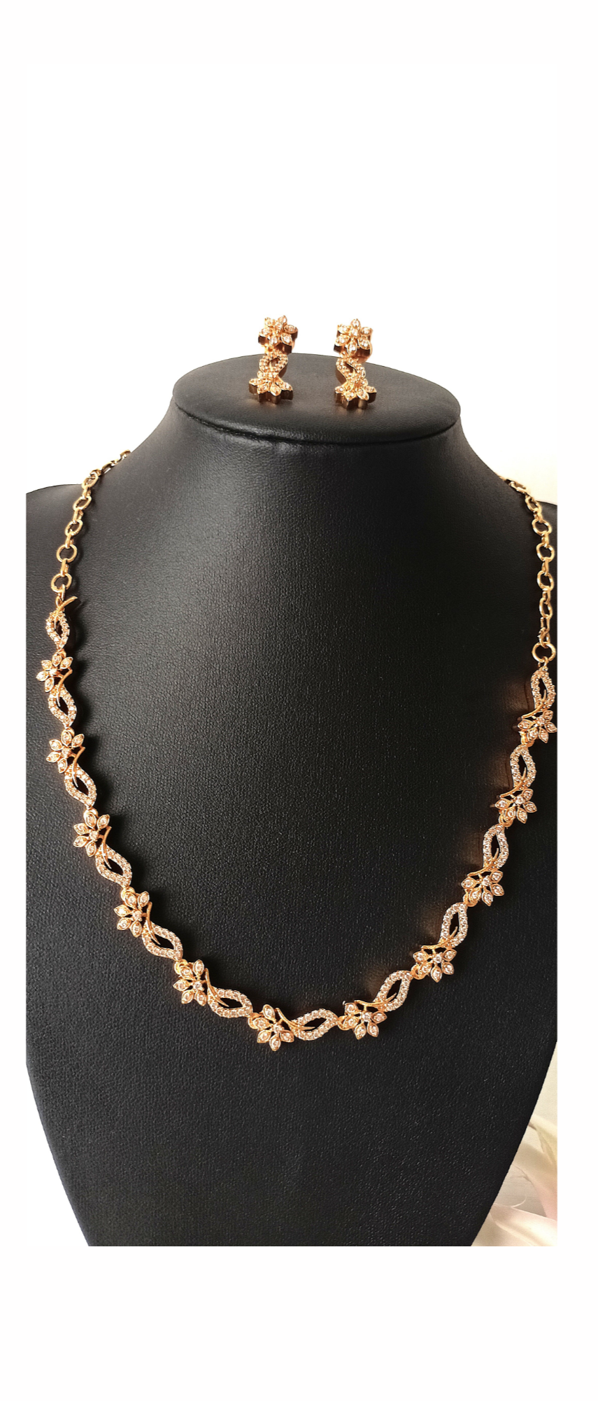 Gold necklace and earrings on a black mannequin bust against a white background
