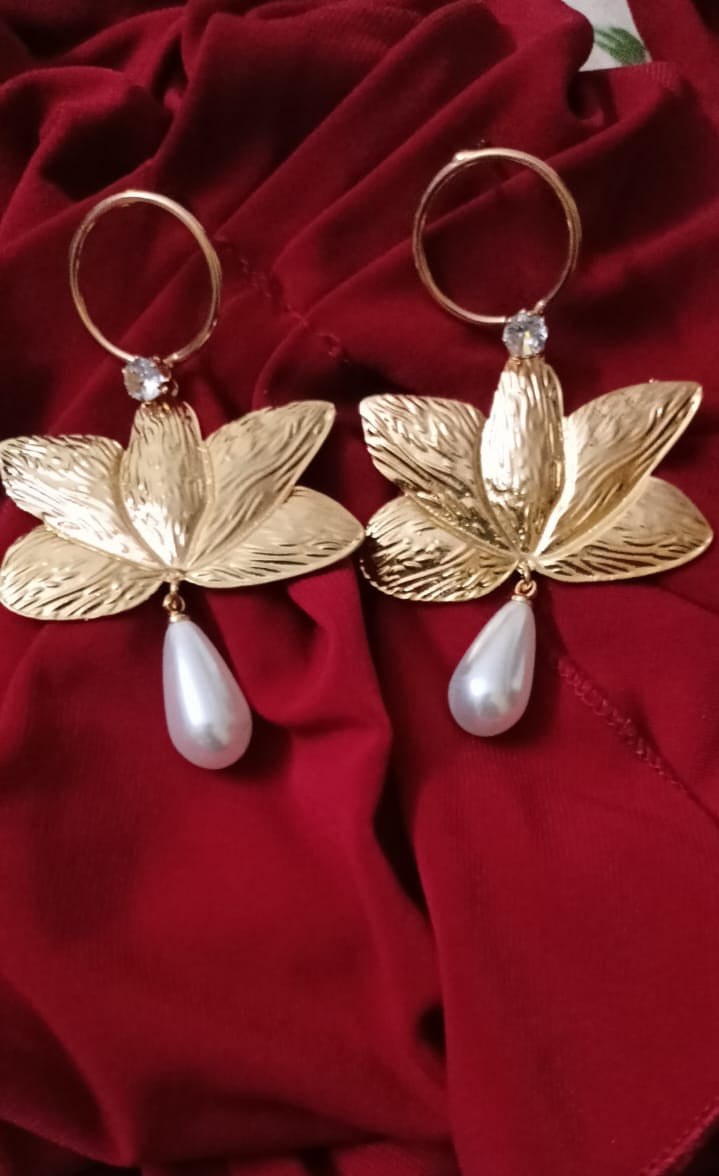 Gold lotus flower earrings with pearl drops on a red fabric background